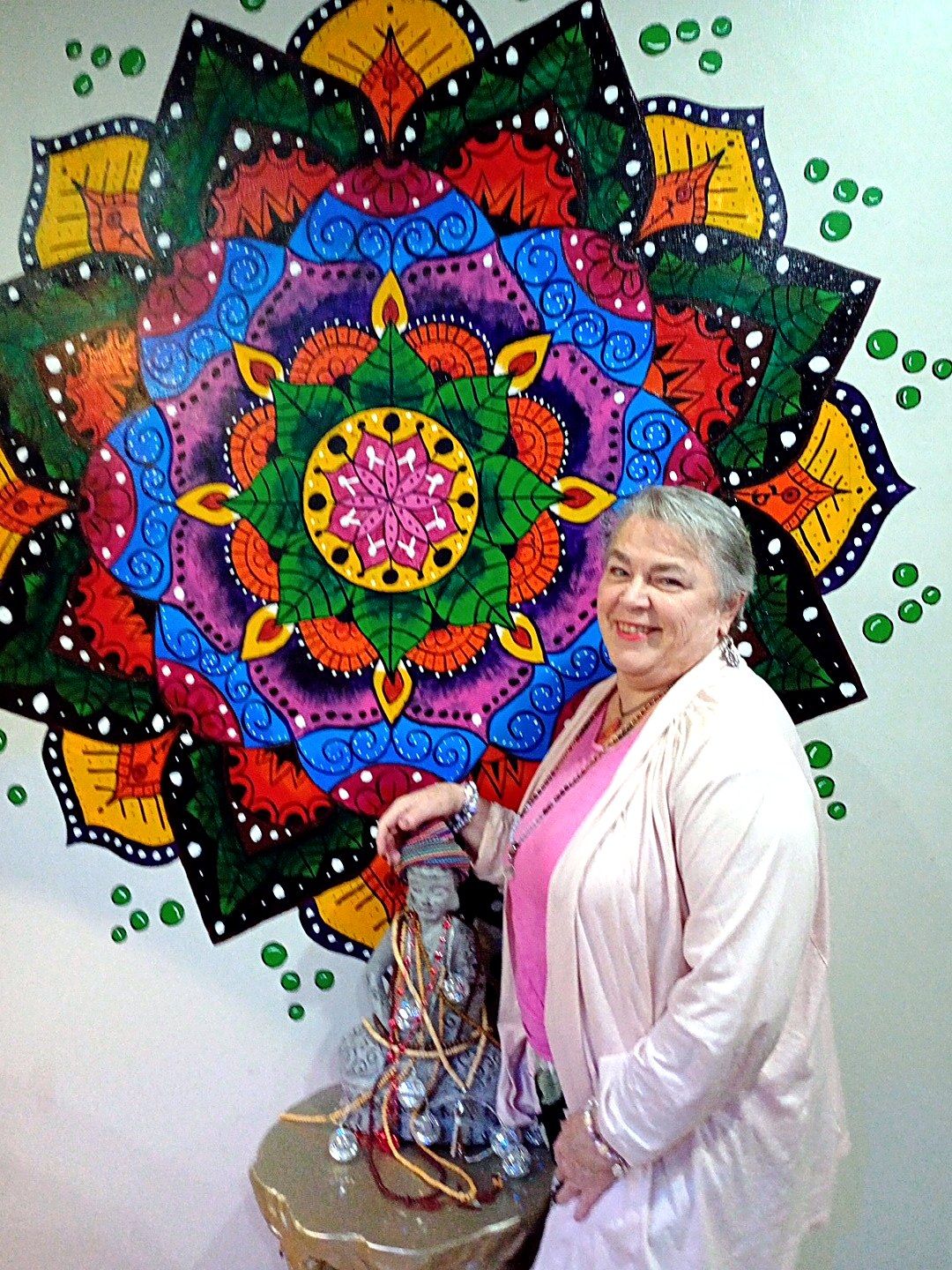 Christine smiling beside a large painted mandala